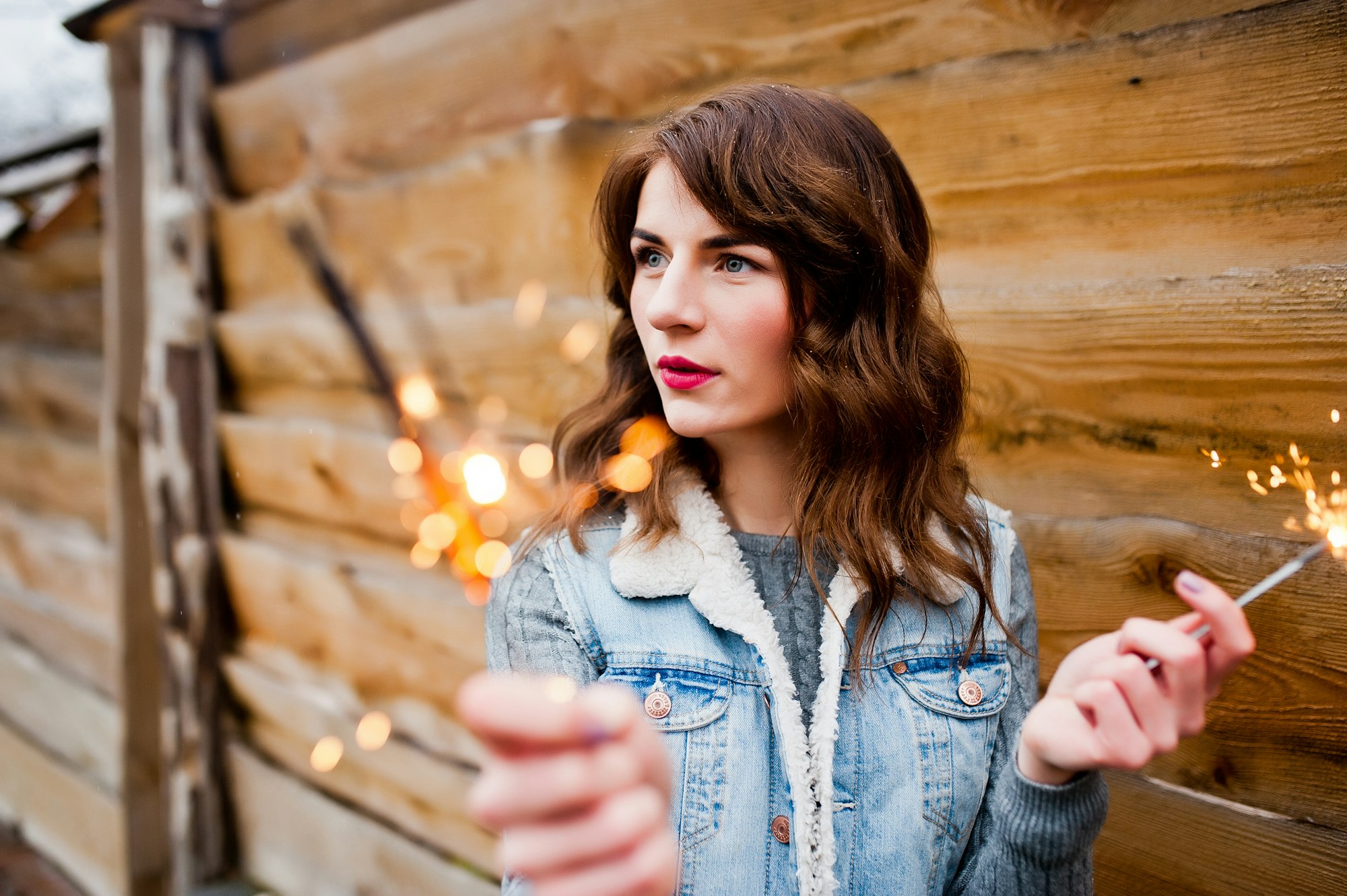 Portrait of brunette girl in jeans jacket with bengal lights in hands.